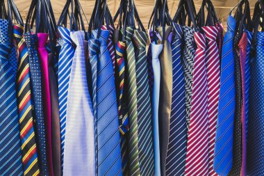 Piyasada satışta asılı renkli kravatlardan oluşan geniş bir koleksiyon. Birçok farklı desenli renkli kravat elbise askılığında asılı. Dükkanda renkli kravat koleksiyonu var. Moda aksesuarı.