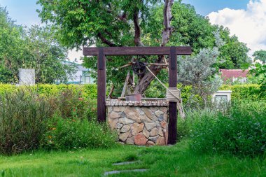 Taş ve tekerlek makara ile yapılmış güzel artezyen metal kova ve halatla huzurlu bahçe atmosferinde. Kırsal alandaki Retro Stone Kuyusu. Antika eşyalarla bahçe dekorasyonu.