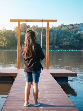 Genç Asyalı bir kadının yaz tatilinde nehir kıyısında tahta bir bankta salıncakta sallanmak için yürüdüğünü görmek. Rıhtımda yapayalnız bir kız ve akşam vakti güzel büyük bir nehirde doğa manzarasının tadını çıkarıyor..