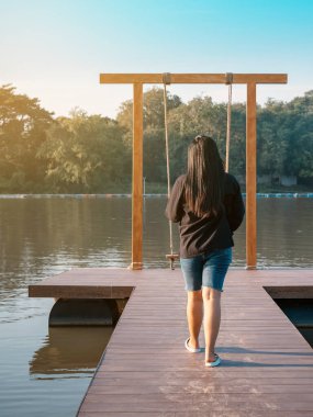 Genç Asyalı bir kadının yaz tatilinde nehir kıyısında tahta bir bankta salıncakta sallanmak için yürüdüğünü görmek. Rıhtımda yapayalnız bir kız ve akşam vakti güzel büyük bir nehirde doğa manzarasının tadını çıkarıyor..