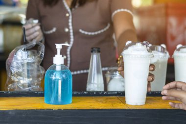 Corona virüsünün (Covid-19) bir hindistan cevizi smoothie dükkanının önünde müşteri hizmetleri için yayılmasını önlemek amacıyla el temizliği için mavi alkol jeli şişesi. Yeni normal yaşam tarzı. Sağlık hizmeti kavramı.