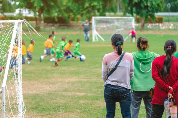 Back view of Moms watch and cheering their sons playing football in school tournament on sideline. Sport, outdoor active,  Spectator watching soccer game. Parents care and encourage their children.