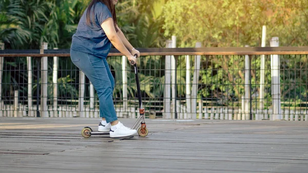 Asian woman enjoy playing and riding modern extreme stunt kick scooter without using any safety gear in home. Active sport lifestyle of young female in nature. Happy woman ride scooter without helmet.