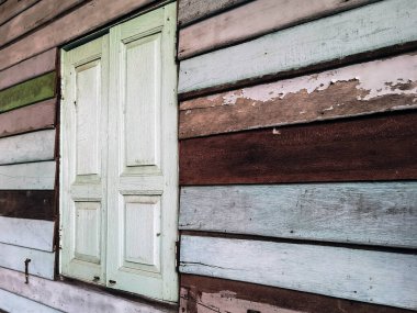 Old grunged wooden window frame painted white vintage with old colourful plywood wall. Antique window frame and old panes. Old closed window and planks of old wooden house. Background of wooden walls
