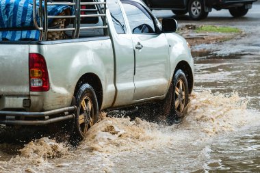 Pickup truck passing through flooded road. Driving car on flooded road during flood caused by torrential rains. Flooded city road with large puddle. Splash by car through flood water. Selective focus.
