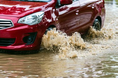 Car passing through a flooded road. Driving car on flooded road during flood caused by torrential rains. Flooded city road with a large puddle. Splash by car through flood water. Selective focus.