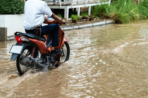 Man ride motorcycle passing through flooded road. Riding motorbike on flooded road during flood caused by torrential rains. Flooded road with large puddle. Splash by motorcycle through flood water.