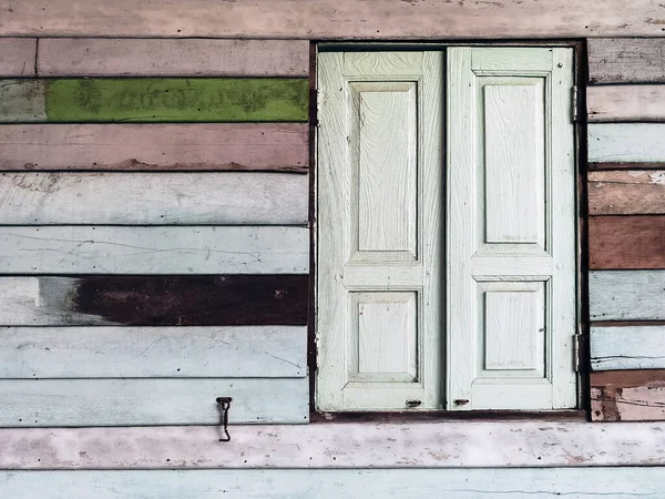 Old grunged wooden window frame painted white vintage with old colourful plywood wall. Antique window frame and old panes. Old closed window and planks of old wooden house. Background of wooden walls