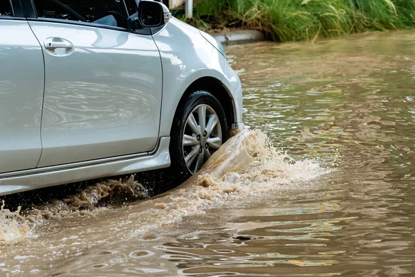 Car passing through a flooded road. Driving car on flooded road during flood caused by torrential rains. Flooded city road with a large puddle. Splash by car through flood water. Selective focus.