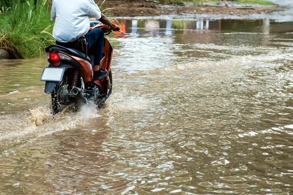 Man ride motorcycle passing through flooded road. Riding motorbike on flooded road during flood caused by torrential rains. Flooded road with large puddle. Splash by motorcycle through flood water.