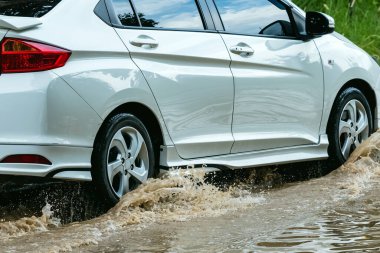 Car passing through a flooded road. Driving car on flooded road during flood caused by torrential rains. Flooded city road with a large puddle. Splash by car through flood water. Selective focus.