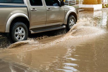 Pickup truck passing through flooded road. Driving car on flooded road during flood caused by torrential rains. Flooded city road with large puddle. Splash by car through flood water. Selective focus.
