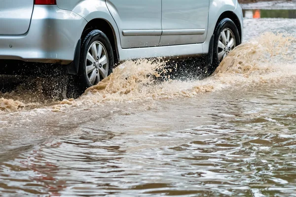 Car passing through a flooded road. Driving car on flooded road during flood caused by torrential rains. Flooded city road with a large puddle. Splash by car through flood water. Selective focus.