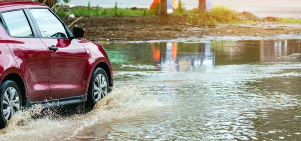 Car passing through a flooded road. Driving car on flooded road during flood caused by torrential rains. Flooded city road with a large puddle. Splash by car through flood water. Selective focus.
