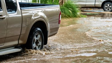 Pickup truck passing through flooded road. Driving car on flooded road during flood caused by torrential rains. Flooded city road with large puddle. Splash by car through flood water. Selective focus.