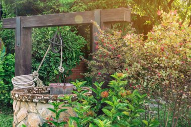 Taş ve tekerlek makara ile yapılmış güzel artezyen metal kova ve halatla huzurlu bahçe atmosferinde. Kırsal alandaki Retro Stone Kuyusu. Antika eşyalarla bahçe dekorasyonu.