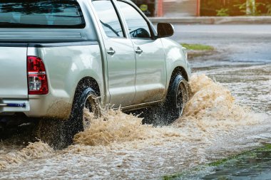 Pickup truck passing through flooded road. Driving car on flooded road during flood caused by torrential rains. Flooded city road with large puddle. Splash by car through flood water. Selective focus.