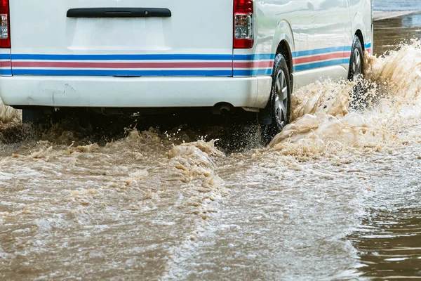 White van passing through flooded road. Driving car on flooded road during flood caused by torrential rains. Flooded city road with large puddle. Splash by car through flood water. Selective focus.
