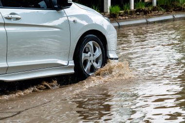 Car passing through a flooded road. Driving car on flooded road during flood caused by torrential rains. Flooded city road with a large puddle. Splash by car through flood water. Selective focus.