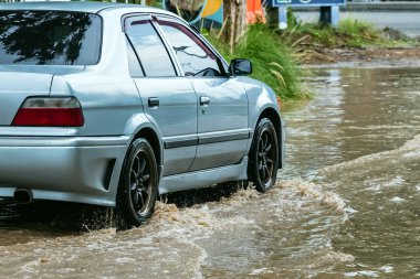 Car passing through a flooded road. Driving car on flooded road during flood caused by torrential rains. Flooded city road with a large puddle. Splash by car through flood water. Selective focus.