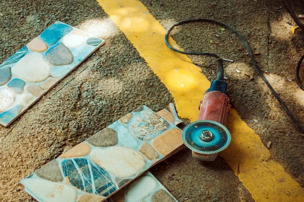 Old red angle grinder with rotary blade on aluminum surface with tiles on floor. Electric angle grinder at construction building site during pavement works. Construction tile cutter industry equipment