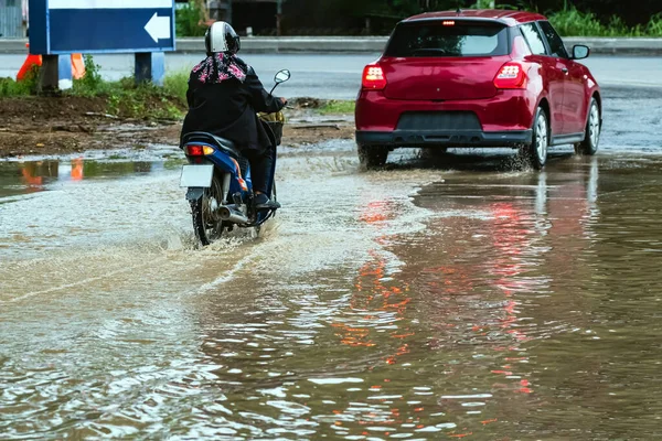 Woman ride motorcycle passing through flooded road. Riding motorbike on flooded road during flood caused by torrential rains. Flooded road with large puddle. Splash by motorcycle through flood water.