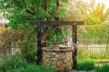 Taş ve tekerlek makara ile yapılmış güzel artezyen metal kova ve halatla huzurlu bahçe atmosferinde. Kırsal alandaki Retro Stone Kuyusu. Antika eşyalarla bahçe dekorasyonu.