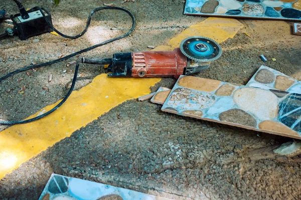 Old red angle grinder with rotary blade on aluminum surface with tiles on floor. Electric angle grinder at construction building site during pavement works. Construction tile cutter industry equipment