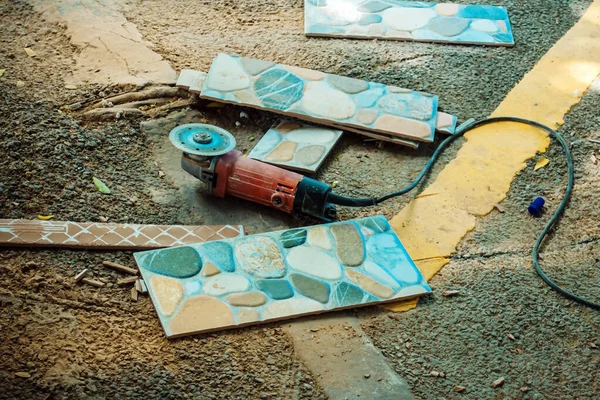 Old red angle grinder with rotary blade on aluminum surface with tiles on floor. Electric angle grinder at construction building site during pavement works. Construction tile cutter industry equipment
