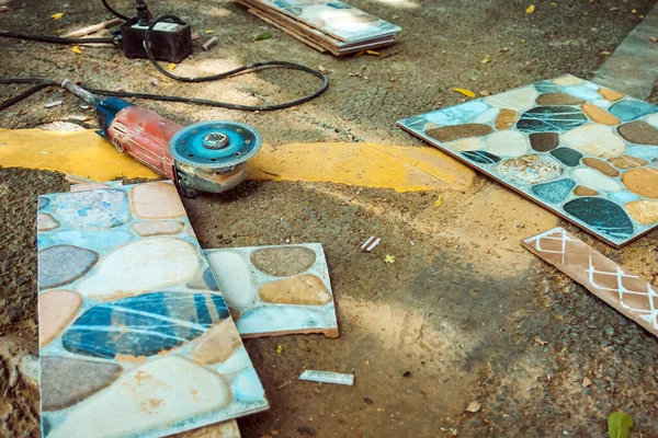 Old red angle grinder with rotary blade on aluminum surface with tiles on floor. Electric angle grinder at construction building site during pavement works. Construction tile cutter industry equipment