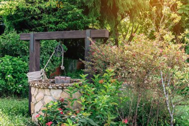 Taş ve tekerlek makara ile yapılmış güzel artezyen metal kova ve halatla huzurlu bahçe atmosferinde. Kırsal alandaki Retro Stone Kuyusu. Antika eşyalarla bahçe dekorasyonu.