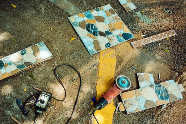 Old red angle grinder with rotary blade on aluminum surface with tiles on floor. Electric angle grinder at construction building site during pavement works. Construction tile cutter industry equipment