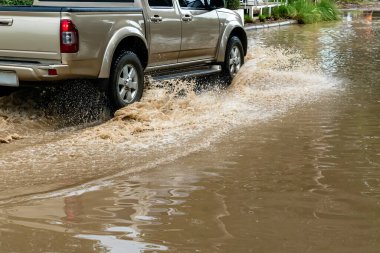 Pickup truck passing through flooded road. Driving car on flooded road during flood caused by torrential rains. Flooded city road with large puddle. Splash by car through flood water. Selective focus.