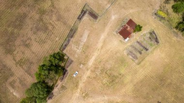 Beyaz bir arabanın yüksek perspektifli drone anteni eski tren raylarının ve tarihi bir teneke barakanın yanına park edilmiş..