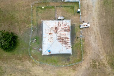 Güvenlik çitleriyle yenilenmiş bir evin paslı beyaz çatısına bakıyorum.