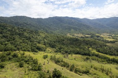 Bulutlu mavi gökyüzünün altındaki bir dağ sırasına doğru vadideki çalılıklar üzerinde hava manzarası yaptım.