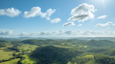Yüksek bulutlar kırsal araziye gölge düşürüyor. Okyanus uzaklarda, sabahın erken saatlerinin puslu sisinde.