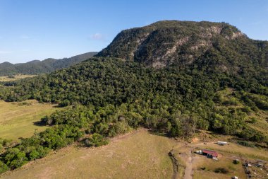 Volkanik çekirdeği kaplayan bir ağaç. Çayırın eteklerinde tarım arazileri ve çiftlikler var.
