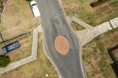Banliyöde, patikaları ve küçük bir trafik adası olan bir mahallede park edilmiş iki aracın tepeden aşağı manzarası.