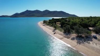 Parlak bir deniz üzerindeki insansız hava aracı Gloucester Queensland Avustralya Burnu 'ndaki Mercan Denizi' nin arka planında dağlar olan kumlu bir sahil beldesine doğru gidiyor.