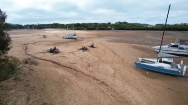 Bucasia Beach, Mackay, Queensland, Avustralya - Haziran 2021: Dalgalar çekildiğinde bir dere yatağında demirlemiş tekneler, kumlu taban, ön planda sürüklenen dallar