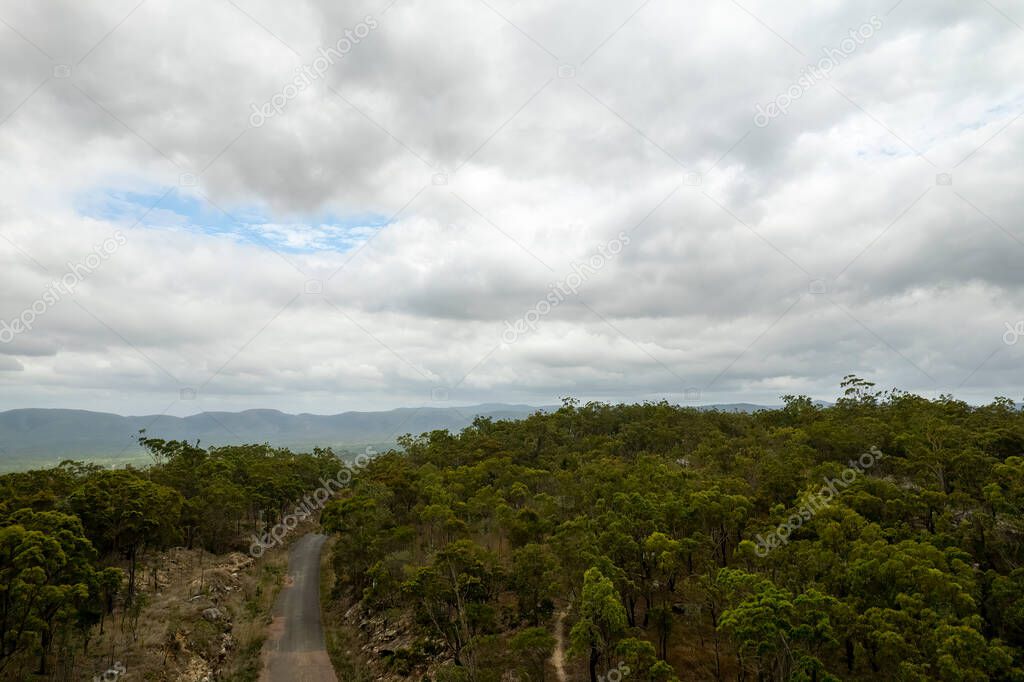 A road meandering through a forest at the top of a mountain range under a cloudy sky