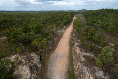 Bir tehlike işaretiyle çalılıklardan geçerek uzaktaki topraklara doğru giden toprak izi.