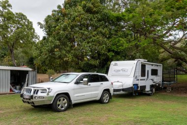 Townsville, Queensland, Avustralya - Kasım 2021: Bir araba ve karavan bir barakanın yanındaki geniş bir ağacın gölgesinde park edilmiş.