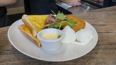 Haşlanmış yumurta, domuz pastırması, balık, tost ve sos büyük beyaz bir yerde servis edilir ve üzeri yeşilliklerle kaplıdır.