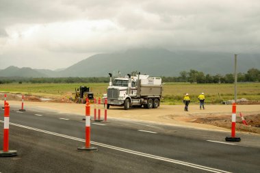 Mackay 'dan Townsville Bruce Highway' e, Queensland, Avustralya - Kasım 2021: İki yol işçisi bir kamyonun yanından geçiyor ve otoyol inşaatında toprak çalışması yapan ağır makineler yapıyorlar