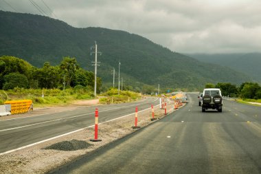 Mackay 'dan Townsville Bruce Highway' e, Queensland, Avustralya - Kasım 2021: Bulutlu bir gökyüzünün altındaki dağ sırasına doğru yol çalışması yapan araçlar