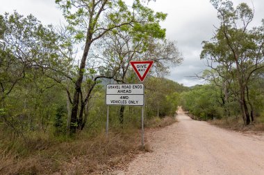 Bir ülke toprak yolunda, çakıllı yolun ileride biteceği ve trafiğe izin verileceği uyarısı