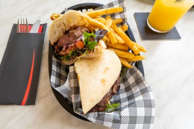 Öğle yemeğinde cips ve portakal suyu ile biftekli sandviç.