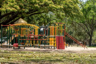 Çocuklar için büyük gölgeli ağaçların altında bir çocuk parkı. Çocuklar için tırmanış, kayma ve sallanmanın eğlencesi.